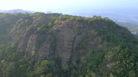 Aerial-view-of-huge-rock-mountain-overgrown-with-green-trees