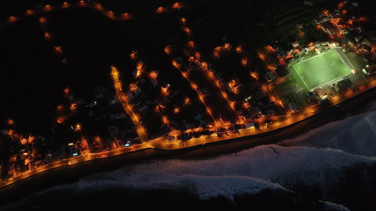 Experience the magic of Madeira at sunset with this aerial video, as the waves crash against the shore and the lights of the city reflect on the water, creating a stunning evening scene