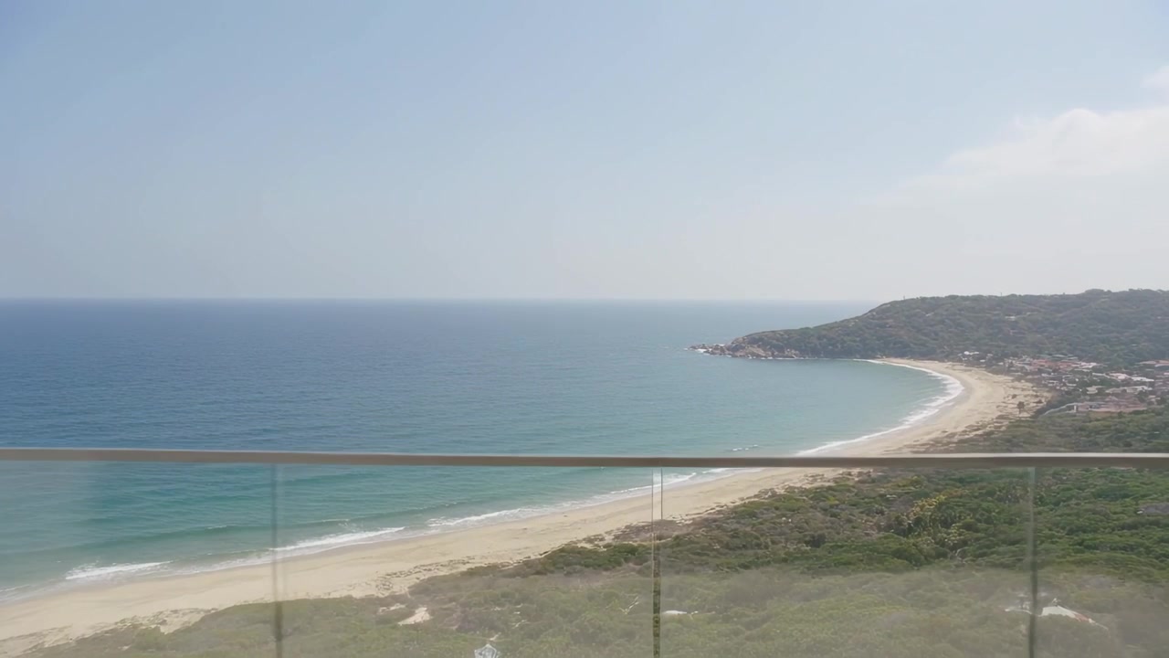 Cortinas transparentes esvoaçando com a brisa entrando, porta de correr abrindo, vista da varanda mostrando o mar.