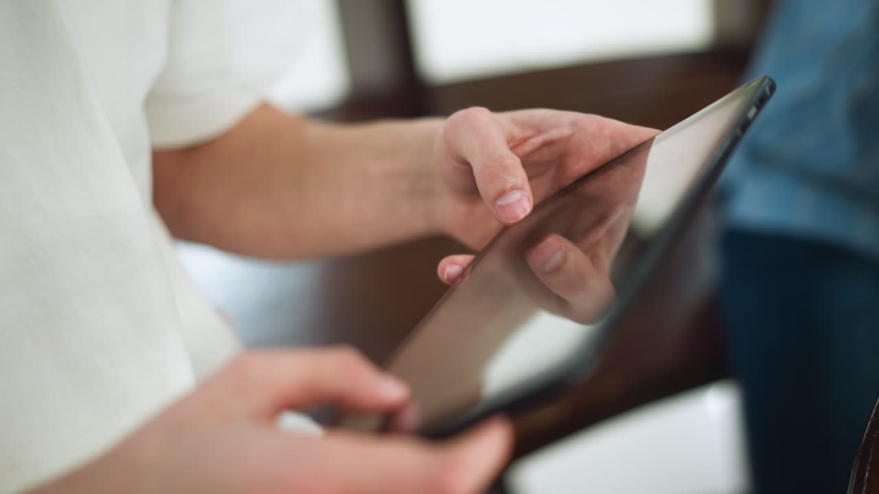White man wearing white polo tapping tablet screen highlighting sunlike symbol on thumbnail nails in modern workspace close up capturing fingertip gesture on touchscreen interface interaction