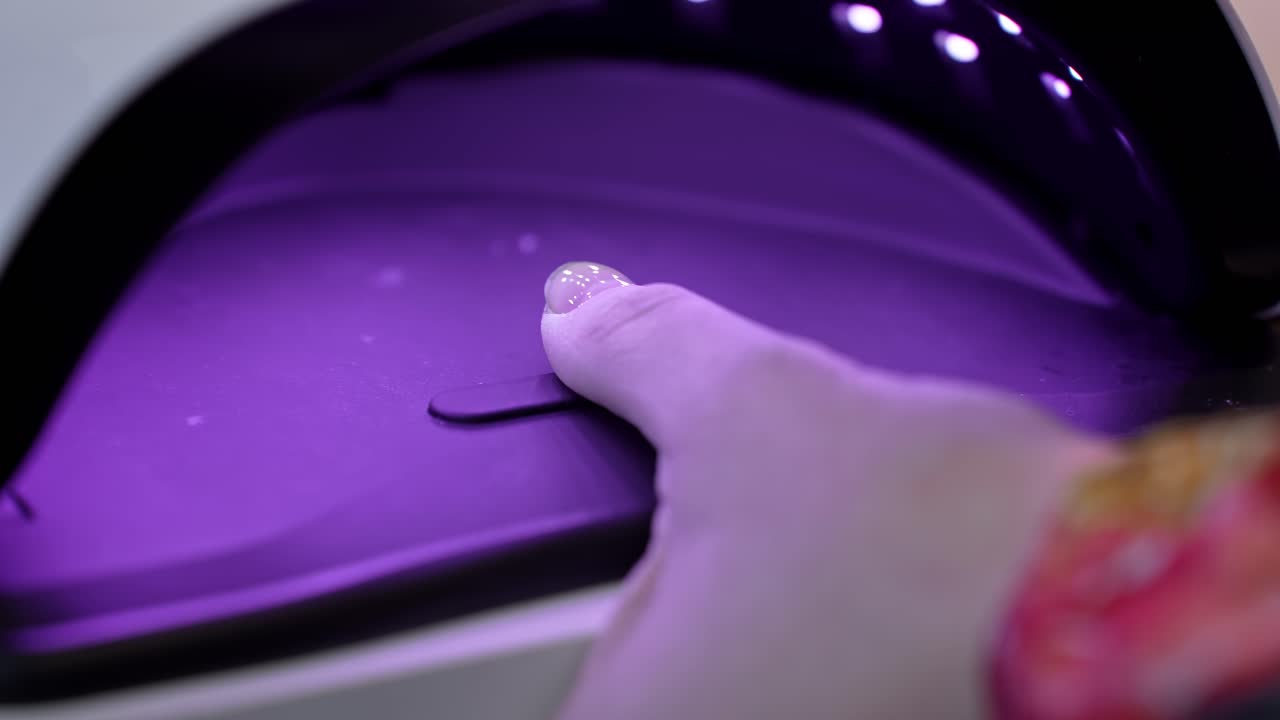 Glitter accent thumb curing under a UV LED nail lamp, glowing in violet light during the final stage of a professional salon manicure