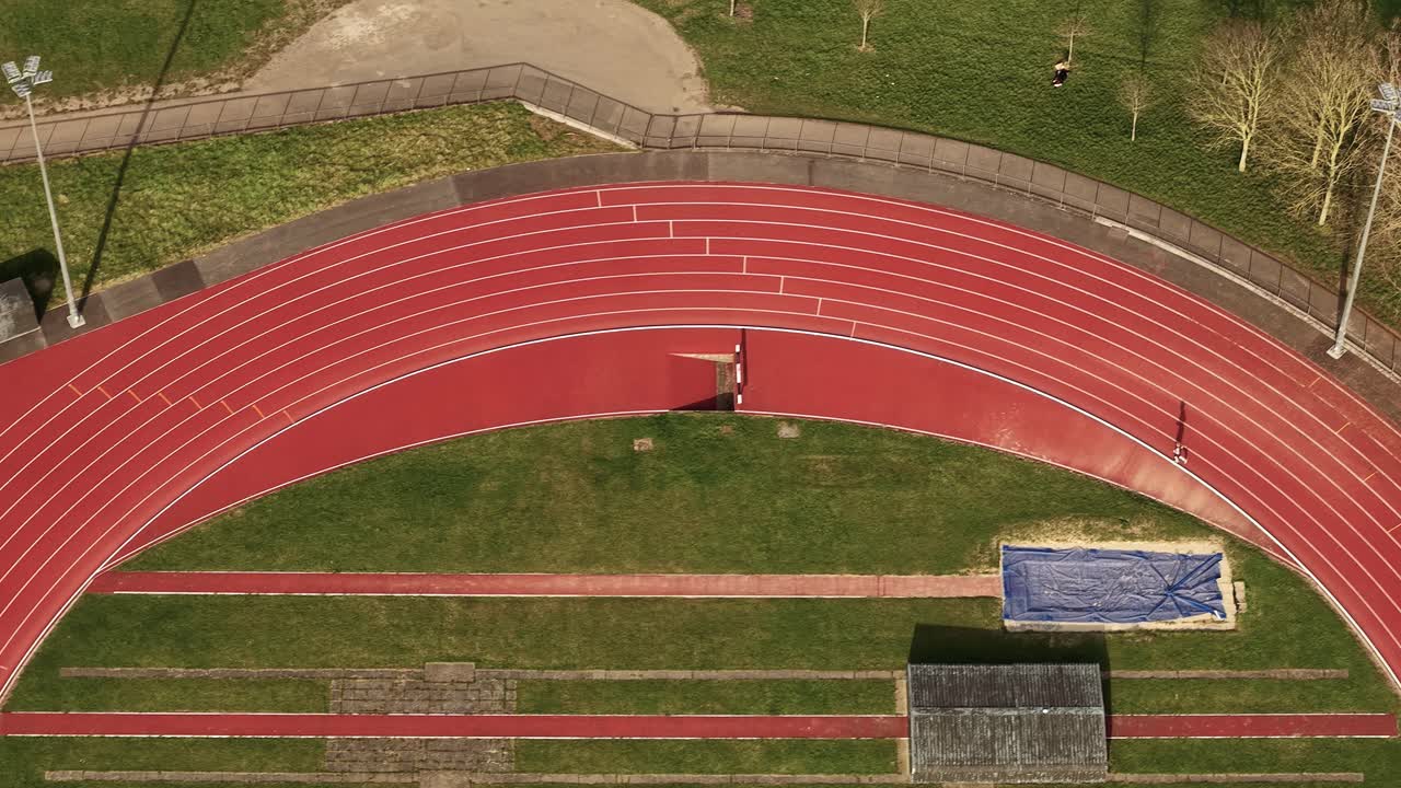 Aerial view following solo runner on red running track in Parliament hill London oval landmark