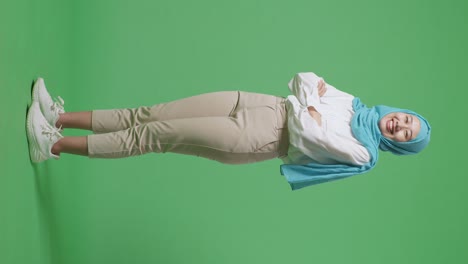 full body of side view of asian muslim woman smiling and crossing her arms while standing in the green screen background studio