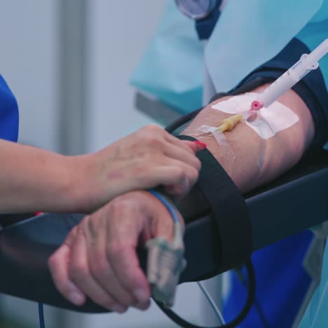 patient's arm with syringe in clinic. medical nurse stands near the patient's hand with pipes during the surgical procedure. close-up. healthcare concept.