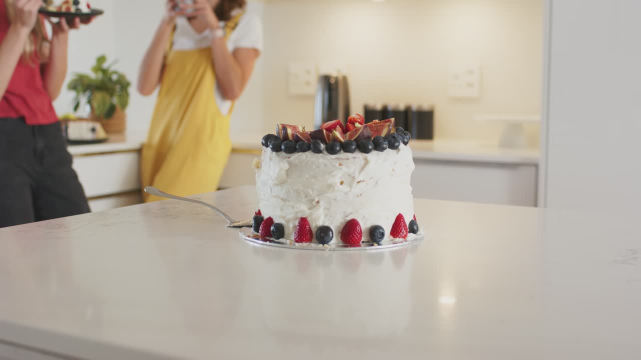 Amiche che notano una torta alla crema di burro in cucina, la fotografano con il telefono, la tagliano e la assaggiano