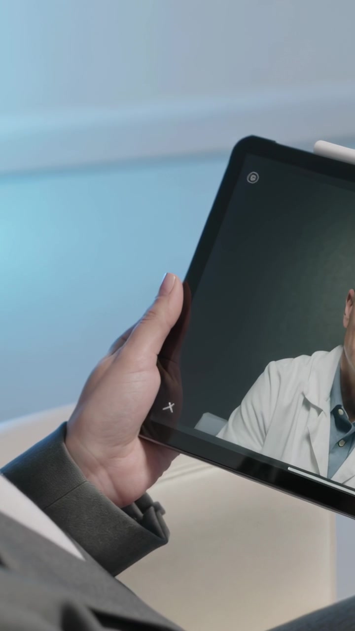 Video verticale: Chi riceve una chiamata stabilizza un tablet in clinica, mostrando camice bianco e stetoscopio.