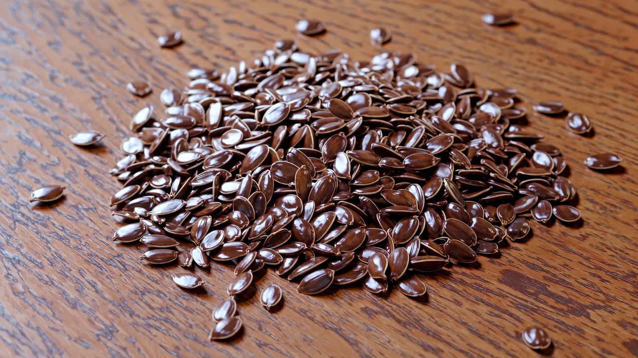 Close-up video shot of flax seeds scattered on a wooden surface, captured from a high angle