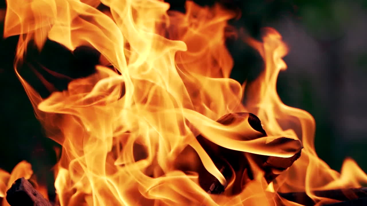 Bright orange flame on blurred background. Vivid flame of firewood burning outdoors. Close-up.