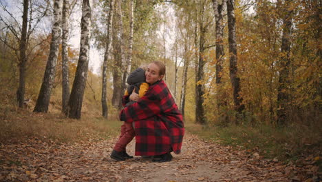 Madre-E-Hijo-Pequeño-Se-Abrazan-En-El-Bosque-De-Otoño-El-Amor-Y-La-Ternura-De-Padres-E-Hijos-En-La-Naturaleza-Caminando-En-El-Parque-Los-Fines-De-Semana