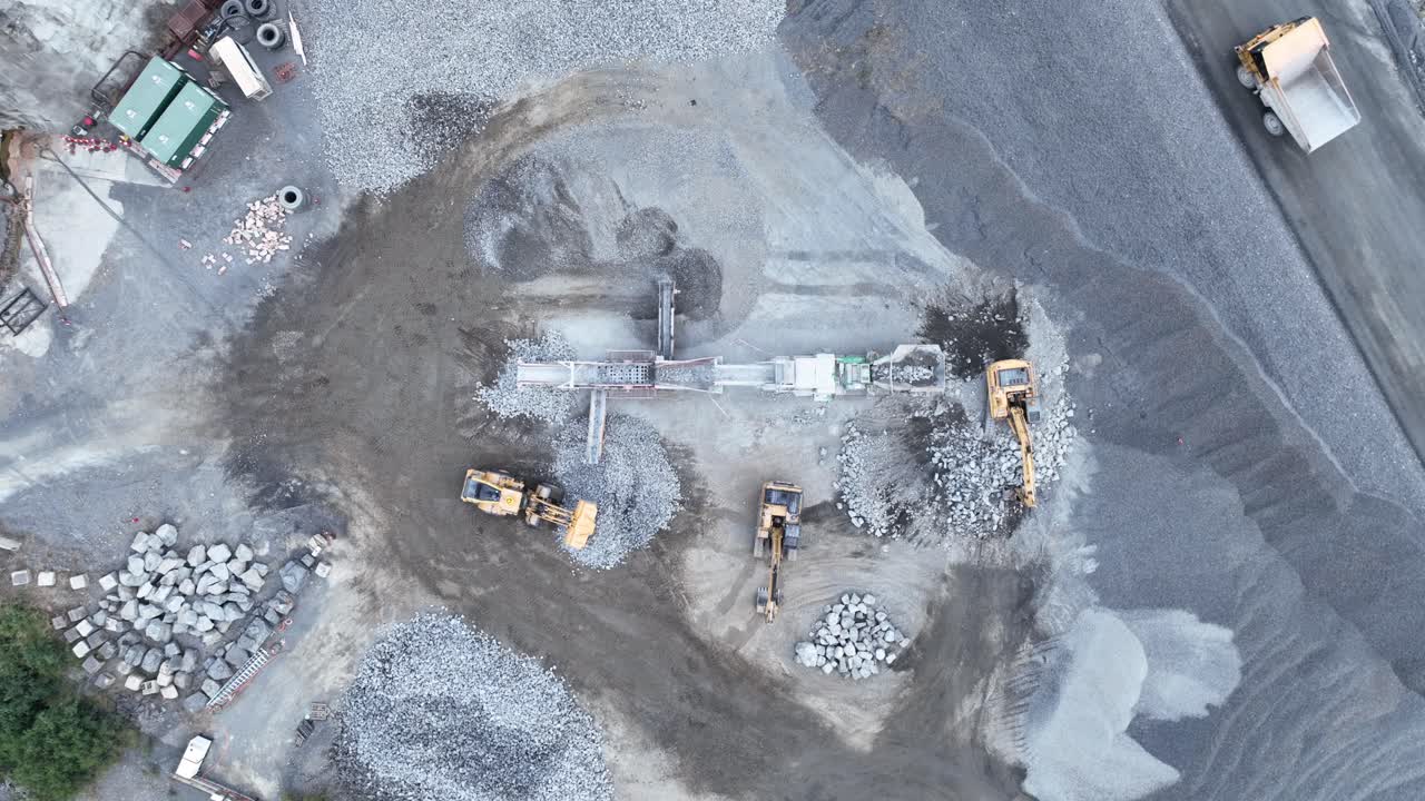 Drone stationary shot of bob cat and mining excavator moving rocks, with conveyor belt sorting rocks with rubble into piles in quarry mine