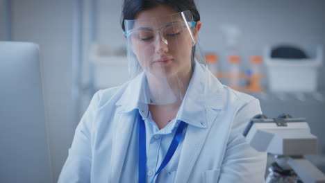 female lab worker wearing ppe face shield recording test results on computer