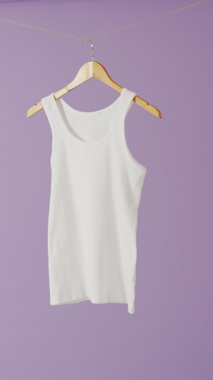 Vertical video of close up of white vest hanging on purple background with copy space