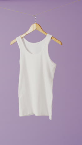 vertical video of close up of white vest hanging on purple background with copy space