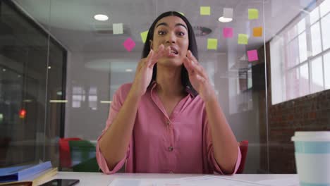 mixed race businesswoman sitting at desk in meeting room having video call and gesturing