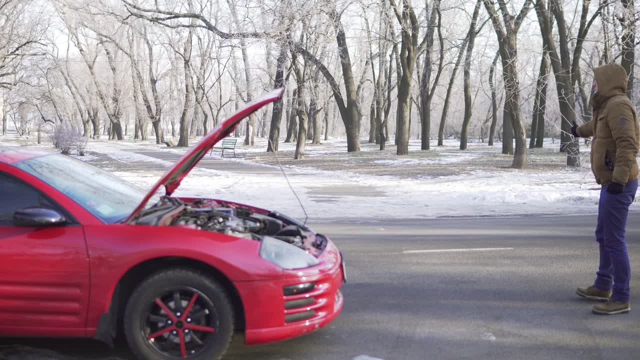 un joven atractivo haciendo autostop en una carretera con su coche averiado cerca de él