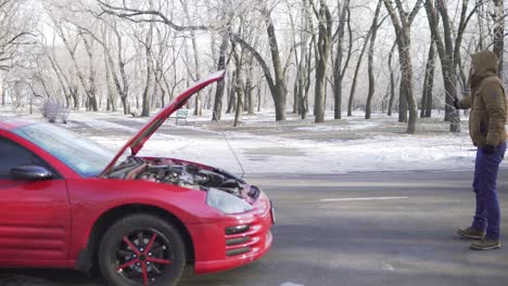 un joven atractivo haciendo autostop en una carretera con su coche averiado cerca de él