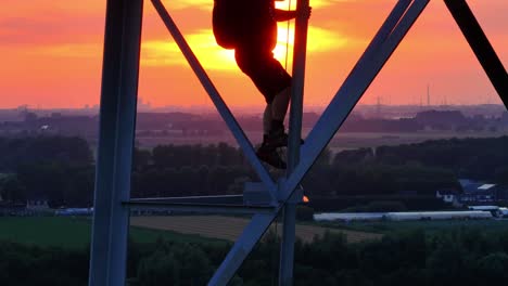 person climbing a tall metal structure at sunset with a glowing sky in the background