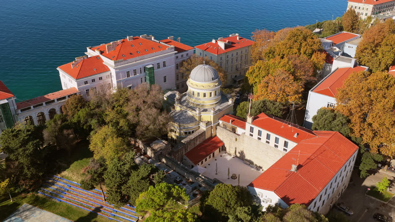 Aerial drone view of the University of Zadar campus and the historic Scientific Library dome surrounded by red roofed buildings and lush autumn trees