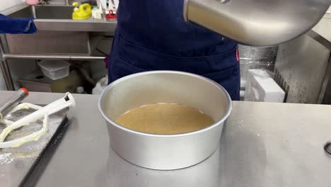 baking paper placed at the bottom of cake mould, professional pastry chef scarping matcha cake mixture using spatula and pouring into baking mould, close up shot of delicious cake making in progress