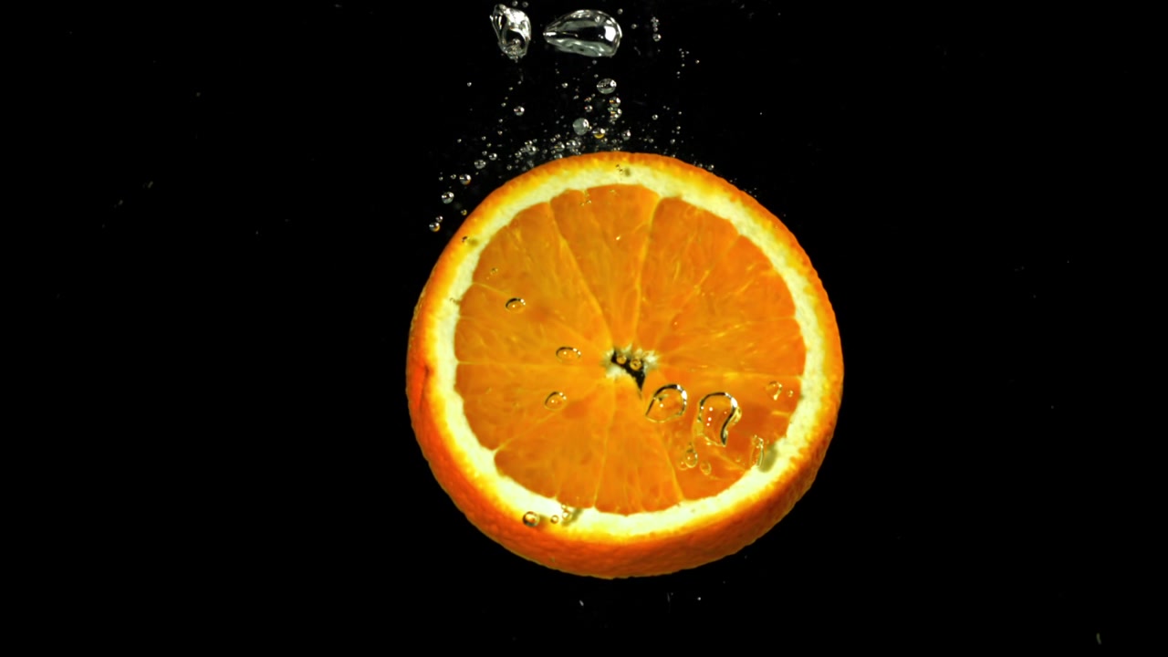 Fetta d'arancia che cade nell'acqua al rallentatore con bollicine