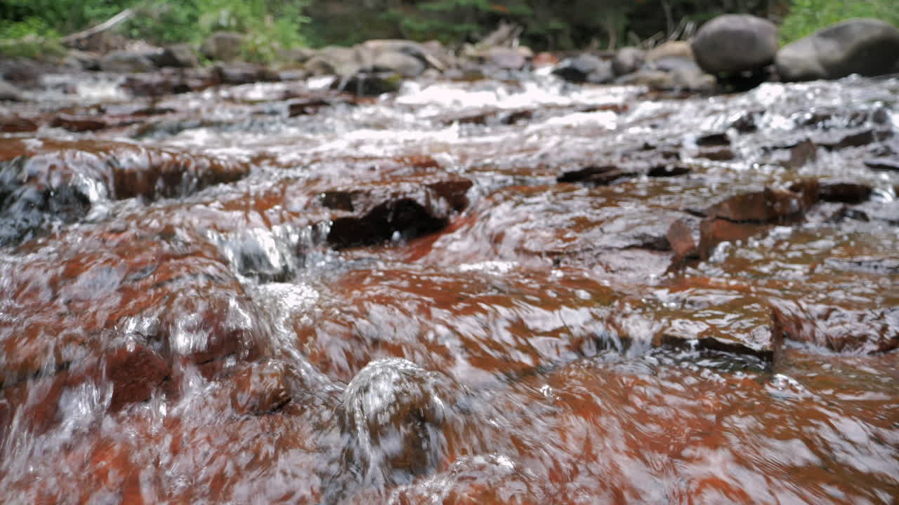 río en cámara lenta que fluye sobre el primer plano de rocas rojas