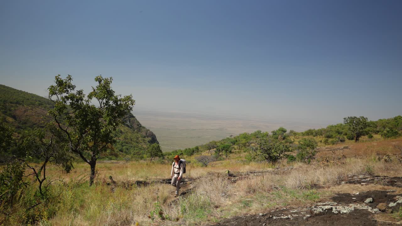 западный турист поднимается на вершину горы в жарком солнце в восточной африке с великолепными видами