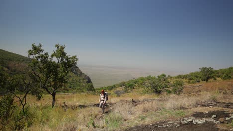 a western hiker climbs along a mountain top in the hot sun in east africa with great views