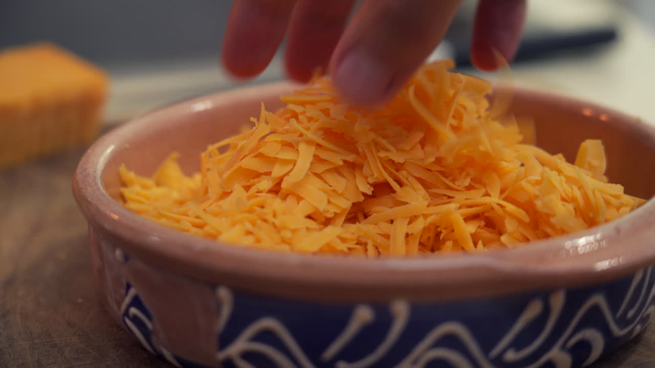 chef mezclando a mano un montón de queso cheddar recién rallado