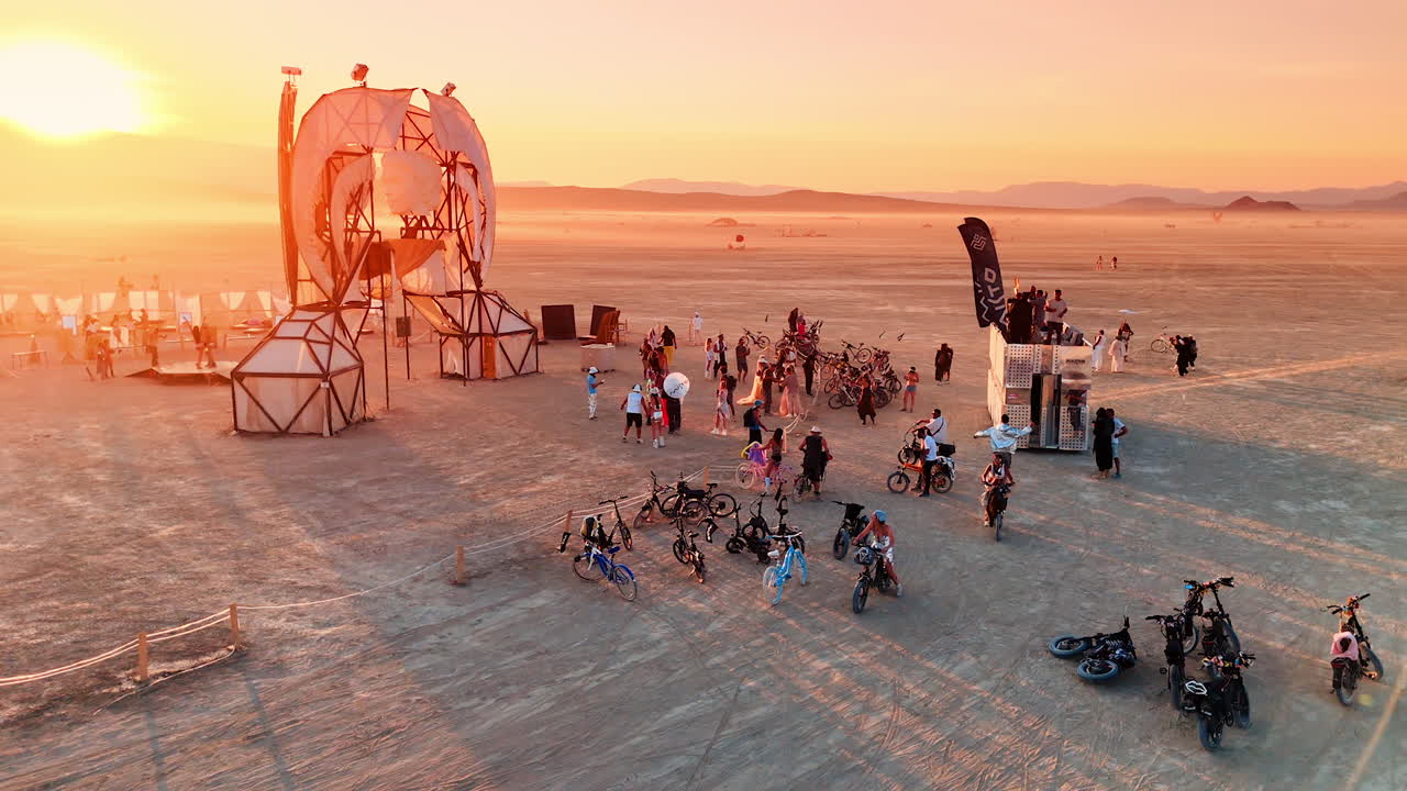 Festival art and bikes in warm desert light. People interact around sculptures and parked bikes as the glowing sunset colors stretch across the playa
