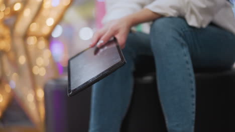 close-up of lady holding and gently moving tablet, focusing on casual interaction with technology, stylish composition highlights denim outfit, sneakers, with soft background lighting and reflections