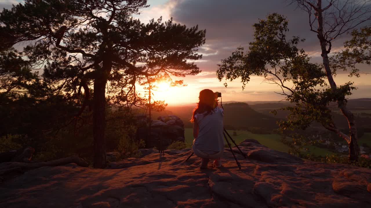 Shot of a photographer taking pictures at sunset with her camera on a tripe in the mountains