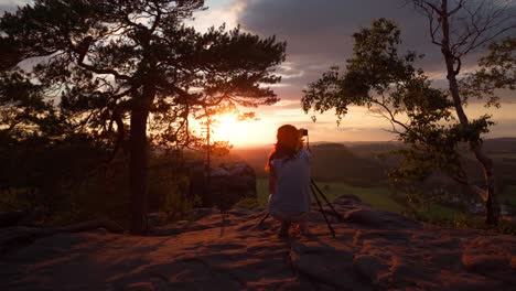 shot of a photographer taking pictures at sunset with her camera on a tripe in the mountains