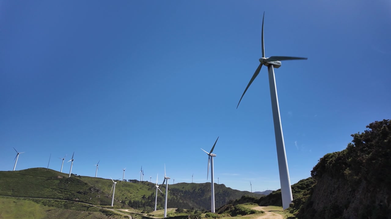 Vista dal basso di turbine eoliche che si ergono sopra una valle di montagna.