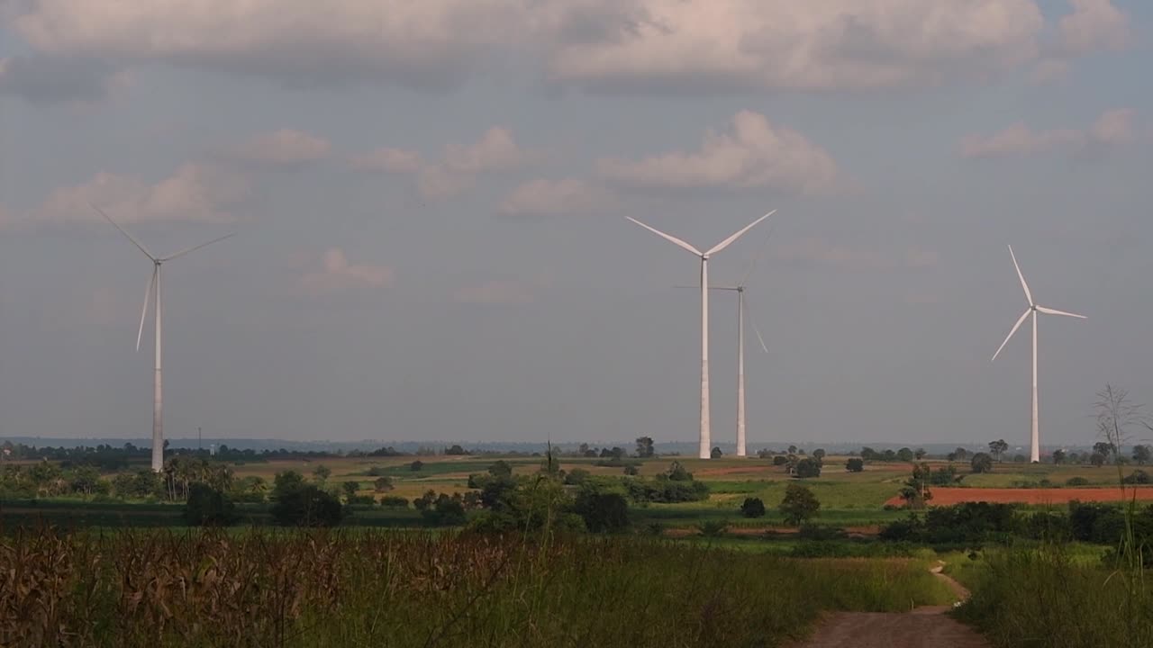 Wind Turbines Towering Farmlands, as farmers grow their crops and tend their animals; clean alternative energy in Thailand and mainland Southeast Asia.