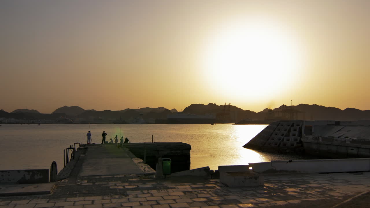Peaceful sunset over the harbor with silhouettes of fishermen and distant cargo ships