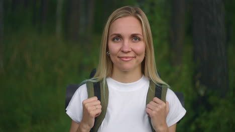 Portrait-of-a-young-woman-traveler-in-the-sun-looking-directly-into-the-camera-and-smiling-flirting-Traveler-with-a-backpack-in-the-Park-and-in-the-woods-in-slow-motion