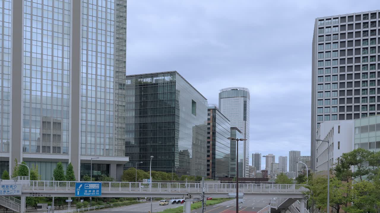 A low-angle shot of a Tokyo cityscape with a variety of modern glass skyscrapers and buildings against an overcast sky