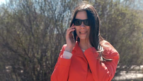 una joven morena con gafas de sol habla por teléfono en el parque de primavera.