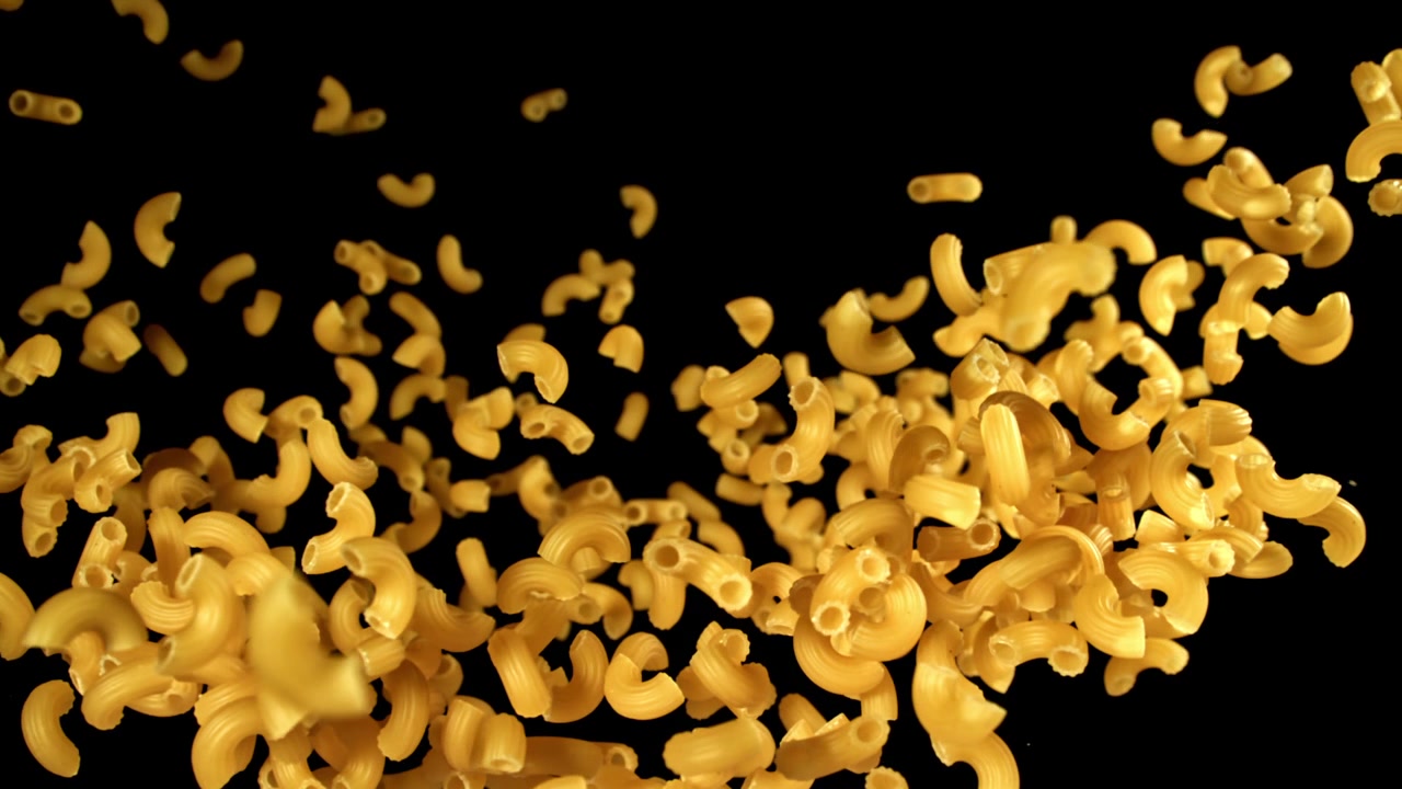 Pâtes macaroni sèches tombant au ralenti sur fond noir