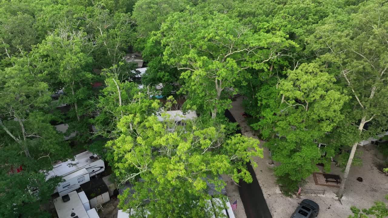 Campground between dense green trees along avenue. Parking camper van and cars. Mobile homes in suburb of American town. Summertime in New Jersey. Aerial Birds Eye shot