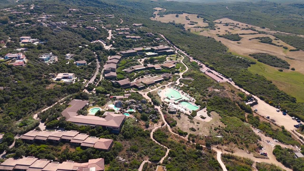 Vista aérea de villas de lujo y piscinas rodeadas de exuberantes colinas y paisaje mediterráneo.