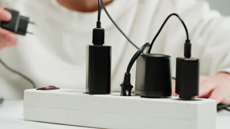 white power strip with many various of cords and cables in close-up. an extension cord with many power sockets. adapter with phone, headphones, usb connectors.tangled wires on table. trying to untangle many messy cables.