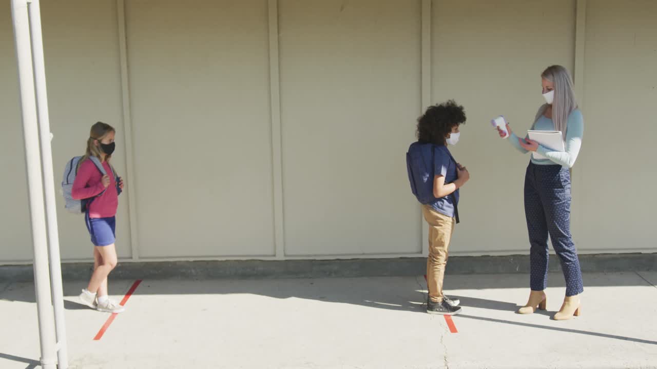 얼굴 마스크 를 착용 한 여자 교사 가 소년 의 온도 를 측정 하고 있다