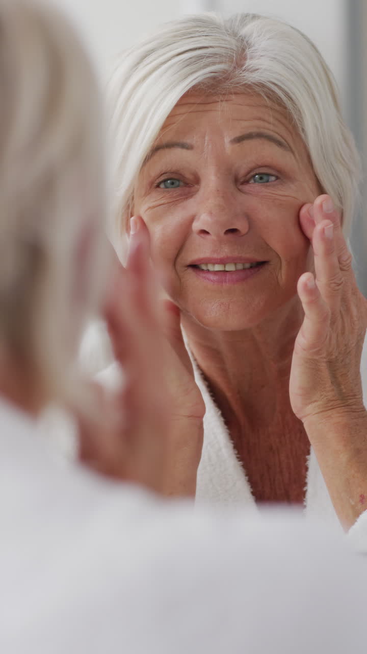 video vertical de una mujer caucásica mayor mirando al espejo en el baño y tocando su cara