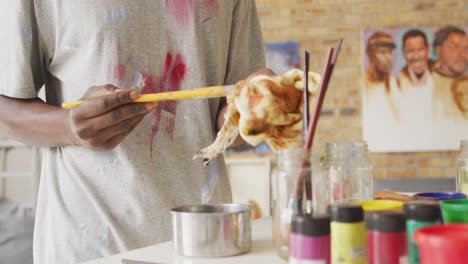 Mid-section-of-african-american-male-artist-cleaning-his-paint-brushes-at-art-studio