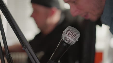 close-up of a microphone in focus with a blurred background featuring a man s hand and part of his face. the scene suggests a studio setting, possibly during a recording session