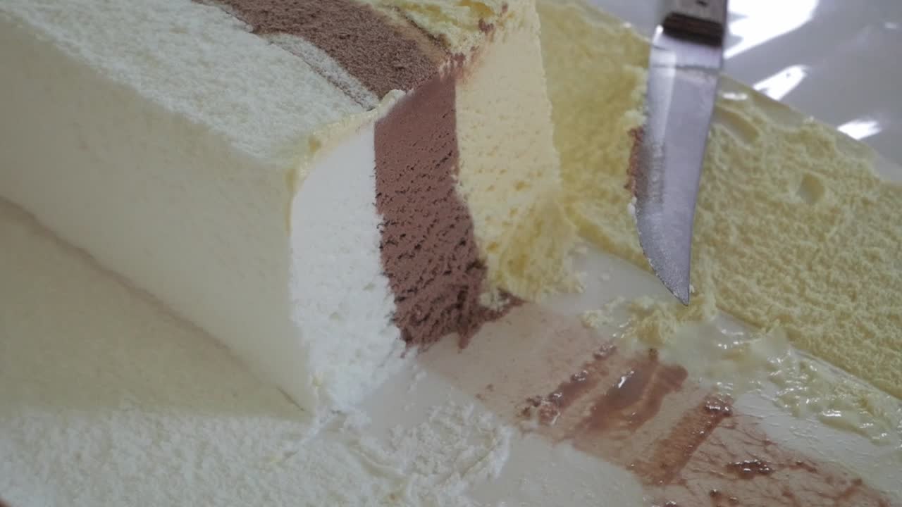Taglio a mano di un sandwich gelato a strati con cioccolato, vaniglia e strati di wafer.