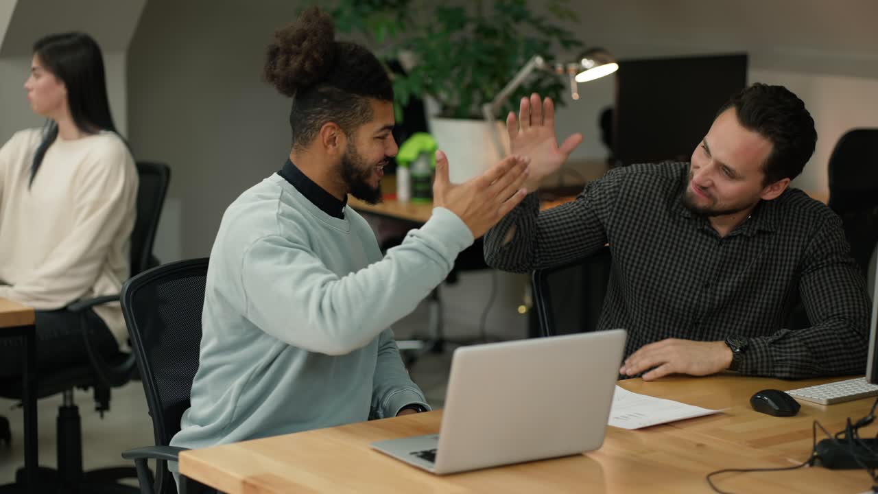 Two male colleagues employees cooperating in office, shaking hands with common result