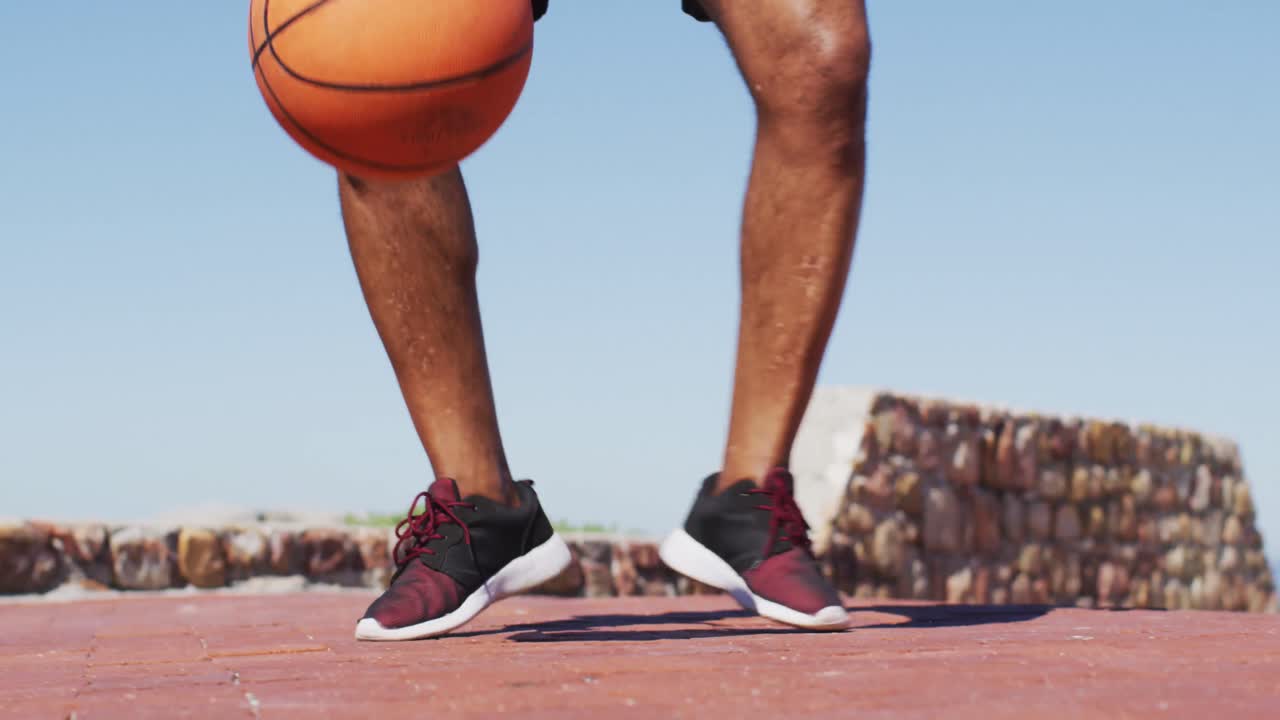 sección baja de un hombre afroamericano mayor jugando al baloncesto en la cancha cerca de la playa