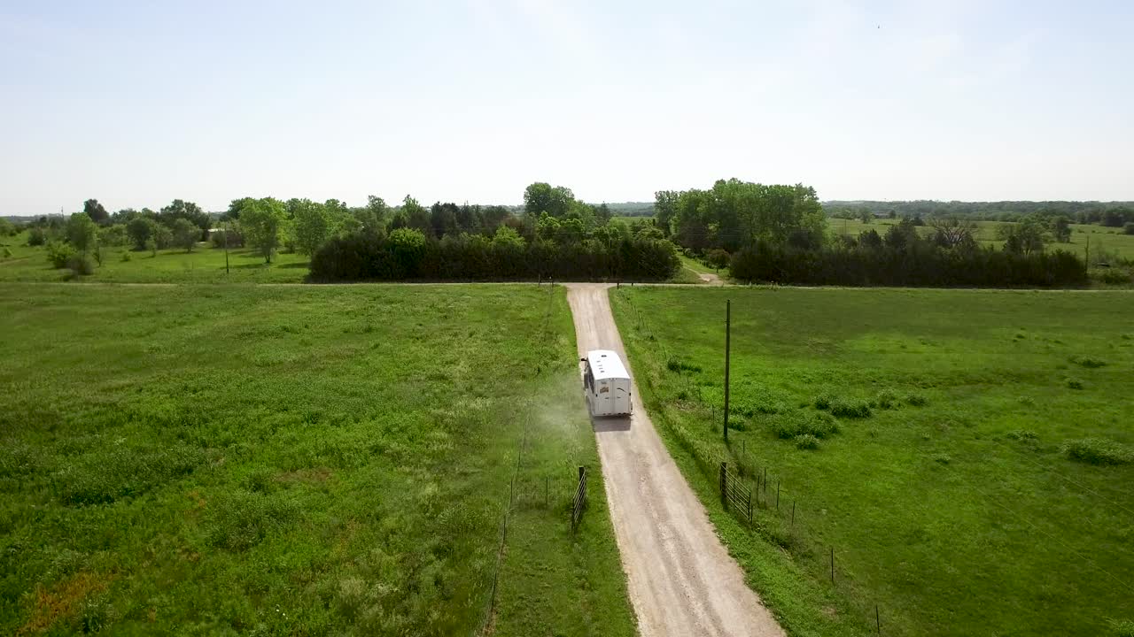 Vista aerea di un grande rimorchio per cavalli, trainato da un pick-up, che percorre una strada sterrata rurale e svolta su un'altra strada sterrata, pronto per un'avventura.